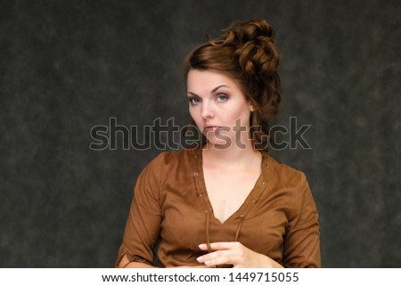 Portrait below breast over gray background of pretty young brunette woman in brown dress with beautiful hair. Standing in different poses, talking, showing with hands, demonstrating emotions.