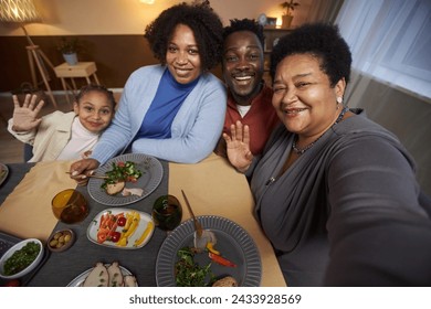 Portrait of big African American family taking selfie photo at dinner table together and waving with grandma holding camera - Powered by Shutterstock