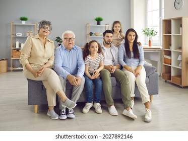 Portrait Of Big Family With Showing Amazed Emotion. Surprised Overwhelmed Grandparents, Parents And Children Sitting On Sofa Being In Shock. Home In Living Room Interior. People Expression