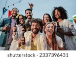 Portrait of a big group of happy young best friends smiling and having fun celebrating a buddies rooftop party, social gathering or birthday meeting at nightime, drinking beer and enjoying together