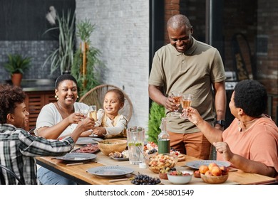 Portrait of big and happy African-American family enjoying dinner together at outdoor terrace with father giving toast - Powered by Shutterstock