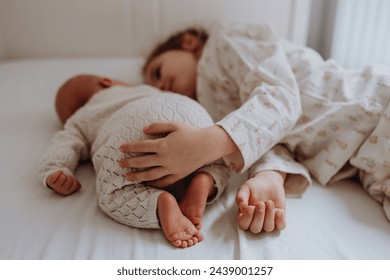 Portrait of big sister cuddling newborn, little baby. Girl lying with her new sibling in bed, closed eyes. Sisterly love, joy for new family member. - Powered by Shutterstock