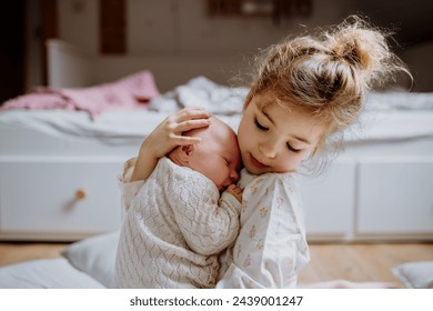 Portrait of big sister holding newborn sister. Girl carefully cuddling small baby. Sisterly love, joy for new family member. - Powered by Shutterstock