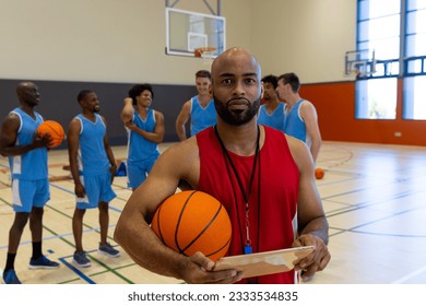 Portrait of biracial male coach with tablet over happy male basketball players talking at gym. Sport, activity, technology, togetherness and lifestyle, unaltered. - Powered by Shutterstock