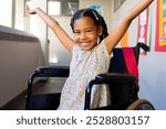 Portrait of biracial schoolgirl sitting in wheelchair with arms wide at elementary school corridor. Disability, education, childhood, development, learning and school, unaltered.