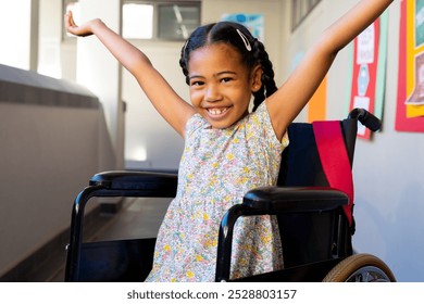 Portrait of biracial schoolgirl sitting in wheelchair with arms wide at elementary school corridor. Disability, education, childhood, development, learning and school, unaltered. - Powered by Shutterstock