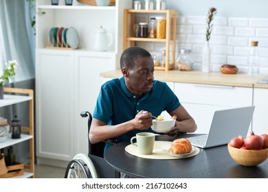 Portrait of black adult man with disability eating breakfast at table in kitchen and watching videos, copy space - Shutterstock ID 2167102643