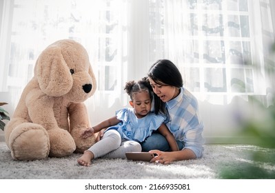 Portrait Of Black African American Family Mother And Daughter Holding A Tablet Smart Phone Looking At It. Asian Little Girl E-learning Together With Mother, Home School. Work From Home Single Mom