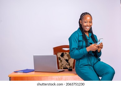 Portrait of a black african happy millennial business woman using her mobile phone and laptop, indoors, at the office.