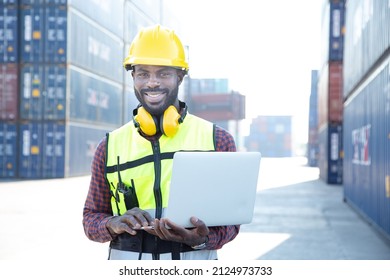 Portrait Black American African Warehouse Staff Wearing Yellow Hard Hat, Construction Vest And Ear Protector Standing With Happy Smile And Checking List Of Container Boxes For Shipping Logistic Stock.