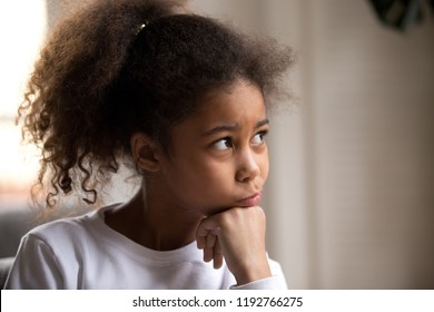 Portrait of black American child with thoughtful face hold hand under chin dreaming and looking away. Serious pensive black African lovely daughter sitting at home feeling boredom or have a question