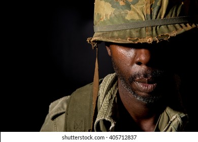 Portrait of a black American G.I.  from the Vietnam War period, with face covered in shadow, against a black background. - Powered by Shutterstock