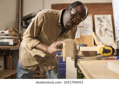 Portrait of Black carpenter blowing sawdust off wooden board while building furniture in workshop - Powered by Shutterstock