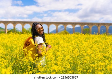 Portrait Of A Black Ethnic Girl With Braids Looking At The Sun, Sunglasses, Traveler, In A Field Of Yellow Flowers