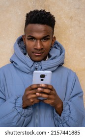 Portrait of a black ethnic man with a phone and a blue jacket on a yellow background, looking at social networks or digital press