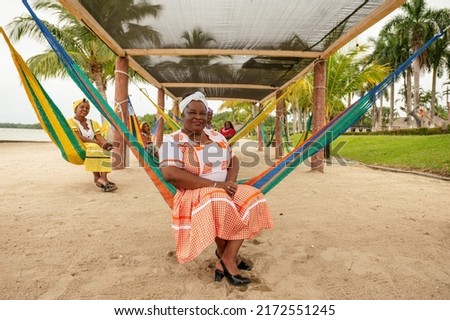 Portrait of a black Garifuna woman looking at the camera sitting in a hammock on the shore of the beach.