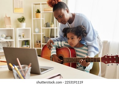 Portrait of black little girl watching online music lesson with mother and playing guitar at home - Powered by Shutterstock