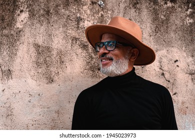 portrait of a black man with a beard and hat leaning against a wall in the street