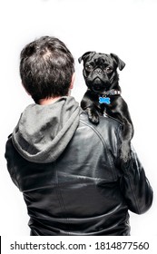  Portrait Of Black Pug And Man, The Pug Is Looking At The Camera In The Arms Of The Owner Who Is Not Facing The Camera, The Owner Has A Black Hoodie.