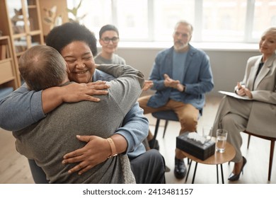 Portrait of Black senior woman embracing friend in group therapy session and smiling happily celebrating recovery, copy space - Powered by Shutterstock