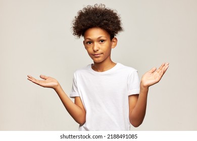 Portrait Of Black Teen Boy In White Mockup T-shirt With Copy Space For Your Advertising Content Raising Hands With Puzzled Unsure Facial Expression Reacting On Question. Doubt Child Concept