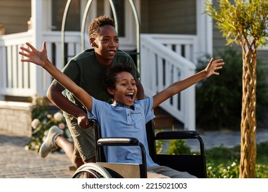 Portrait of black teenage boy pushing littlle brother in wheelchair while having fun together outdoors - Powered by Shutterstock