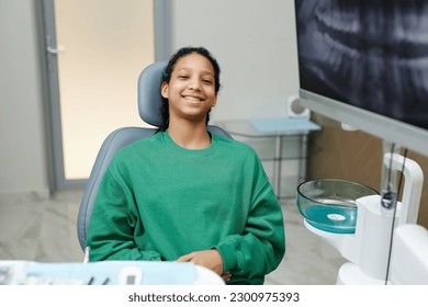 Portrait of black teenage girl sitting in dental chair and smiling at camera - Powered by Shutterstock