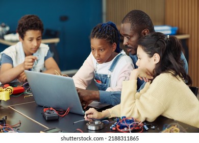 Portrait Of Black Teenage Girl Using Laptop In School During Engineering Class With Male Teacher And Diverse Group Of Children