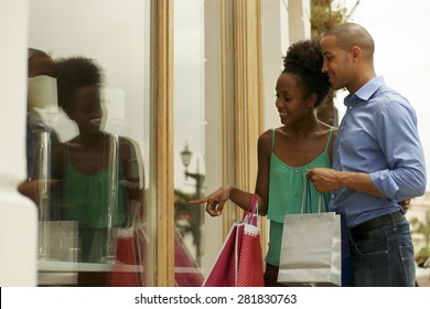 Portrait Of Black Tourist Heterosexual Couple In Panama City With Shopping Bags. The Man And His Girlfriend Look At Shop Window