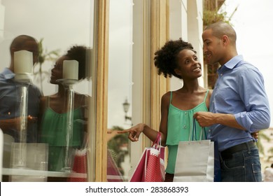 Portrait Of Black Tourist Heterosexual Couple In Panama City With Shopping Bags. The Man And His Girlfriend Look At Shop Window