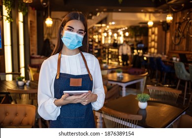 Portrait Of Black Waitress Wearing Protective Face Mask While Holding Touchpad And Looking At The Camera. Happy Waitress Working At A Restaurant And Using A Digital Tablet 