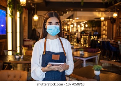 Portrait Of Black Waitress Wearing Protective Face Mask While Holding Touchpad And Looking At The Camera. Happy Waitress Working At A Restaurant And Using A Digital Tablet 