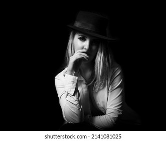 Portrait in black and white monochrome of beautiful blonde woman posing in front of black background with black fedora in sensual glamor lighting