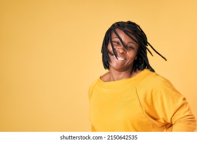 Portrait of a black woman with braided hair dancing. yellow sweater on blue studio background. Copy space