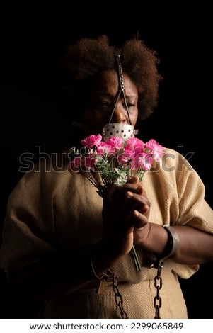Portrait of a black woman with chains on her hands and an iron mask on her face holding a bunch of flowers. Slave Anastacia. Slavery in Brazil.