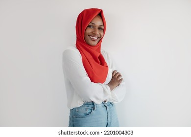 Portrait Of Black Woman In Hijab Posing With Folded Arms On Light Studio Background And Smiling At Camera, Copy Space. Positive Lady Standing Next To Empty Space For Advertisement