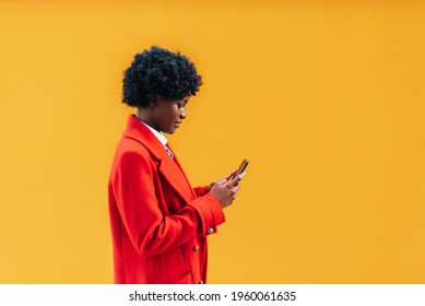 Portrait Of Black Woman With Wavy Hair Holding In Hands Mobile Chat Device Isolated On Bright Yellow Background. Afro Girl Walking With Cell Phone On Plain Background. Horizontal Photo, Copy Space.