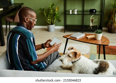 Portrait of black young man holding tablet with blank screen while operating smart home devices in cozy interior with pet dog - Powered by Shutterstock