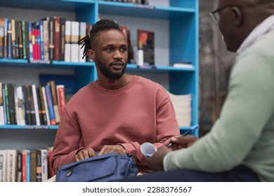 Portrait of black young man talking to therapist of guidance counsellor in college library - Shutterstock ID 2288376567