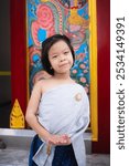 Portrait of A black-haired girl wearing a Thai dress with a silver sash sits smiling happily on the temple terrace while out sightseeing with her family.