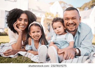 Portrait, blended family and parents on the lawn with their kids in the garden of their home together. Mother, father and children lying on the grass in the yard of their house for love or bonding