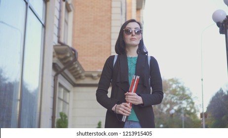 portrait of a blind girl in glasses with a cane on a city street