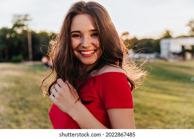 Portrait of blithesome caucasian woman with dark hair standing on blur nature background. Glad brunette girl in red dress smiling to camera during rest in park. - Powered by Shutterstock