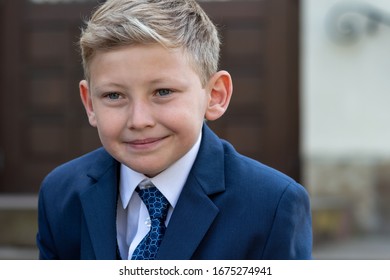 Portrait Of Blond 9 Year Old Boy In Blue Suit Smiling But Not Looking At Camera