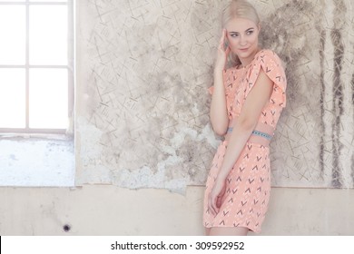 Portrait Of Blond Female In Pink Dress Over Grey Wall.