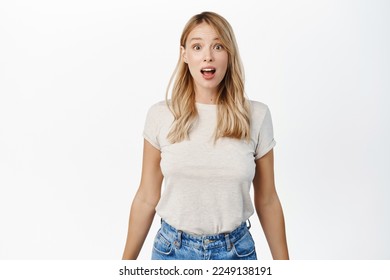 Portrait of blond girl looking surprised and amazed, saying wow, staring with thrilled face expression, white background