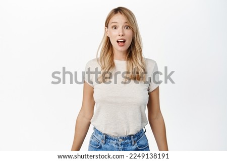 Portrait of blond girl looking surprised and amazed, saying wow, staring with thrilled face expression, white background