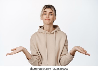 Portrait Of Blond Girl Shrugs, Shows Empty Hands, Apologizing Smile, Stands Against White Background.