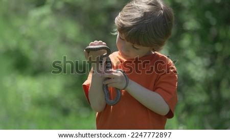 Portrait of blond hair child hold and look at snake, little boy catch dangerous