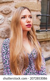 Portrait of blond latin woman with scar on cheek and wearing stylish floral dress leans against the wall in the street. Face shot of beautiful argentinian girl. Face shot, lifestyle concept.